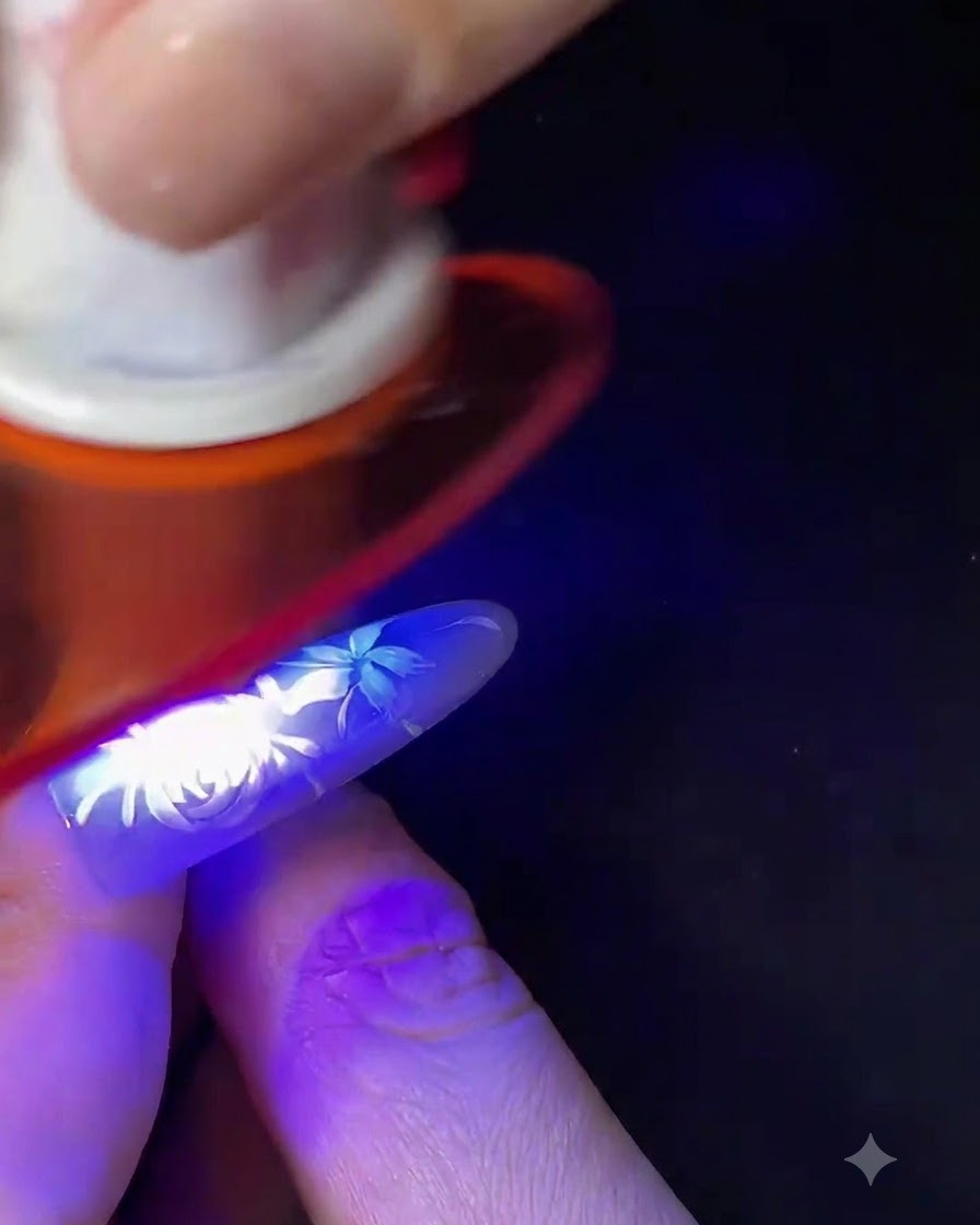 Un doigt avec un nail art floral blanc en cours de catalysation sous une petite lampe UV/LED bleue.