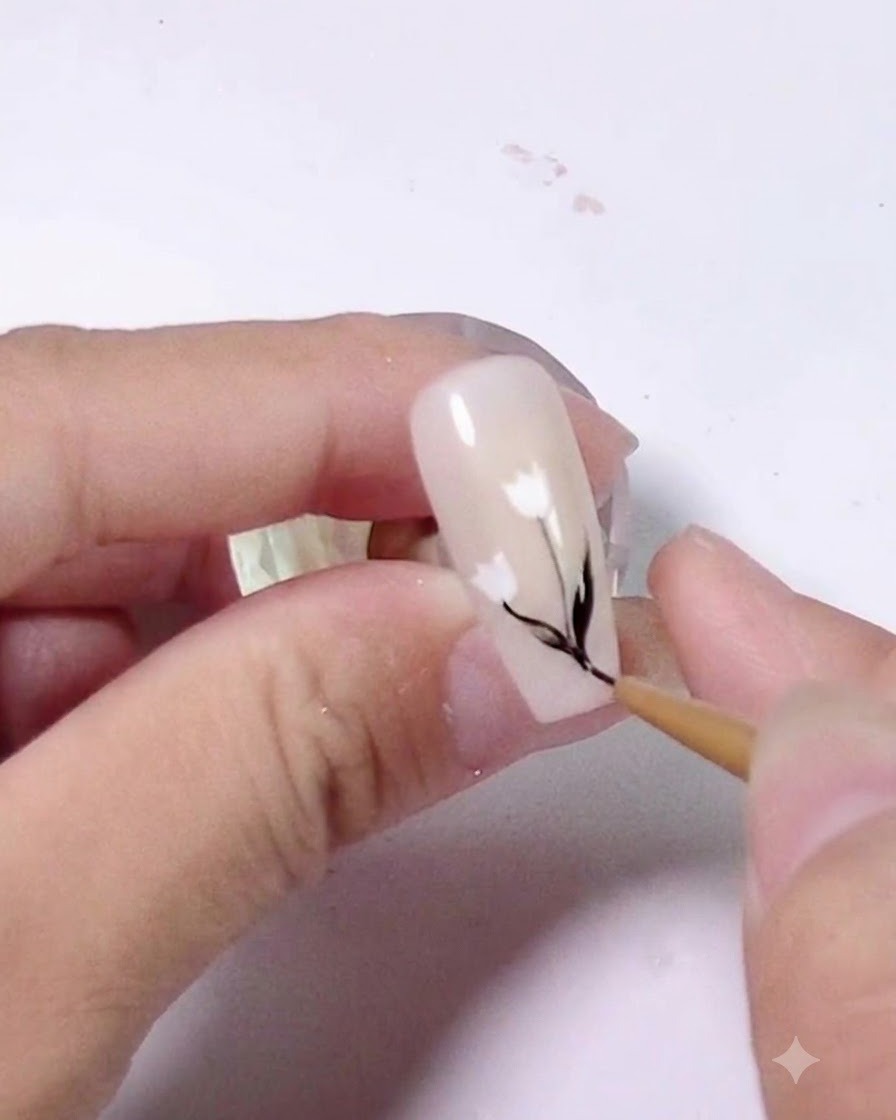 Gros plan montrant lajout de petits détails de feuilles noires le long de la tige dun ongle décoré.