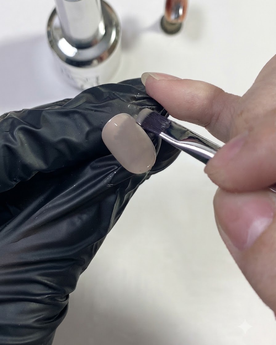 Une main gantée appliquant une couleur de base nude sur une capsule dongle.