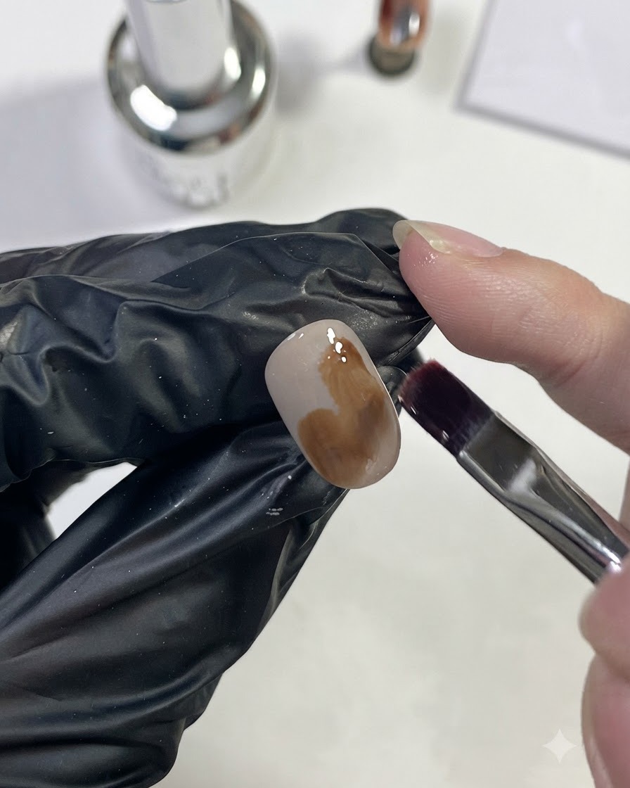 Un pinceau à ongles appliquant du gel brun caramel clair en grande tache sur longle.