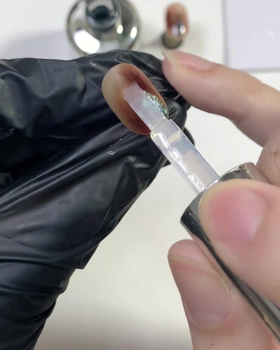 Un pinceau glissant une couche généreuse de top coat transparent brillant sur longle ambre œil-de-chat fini.