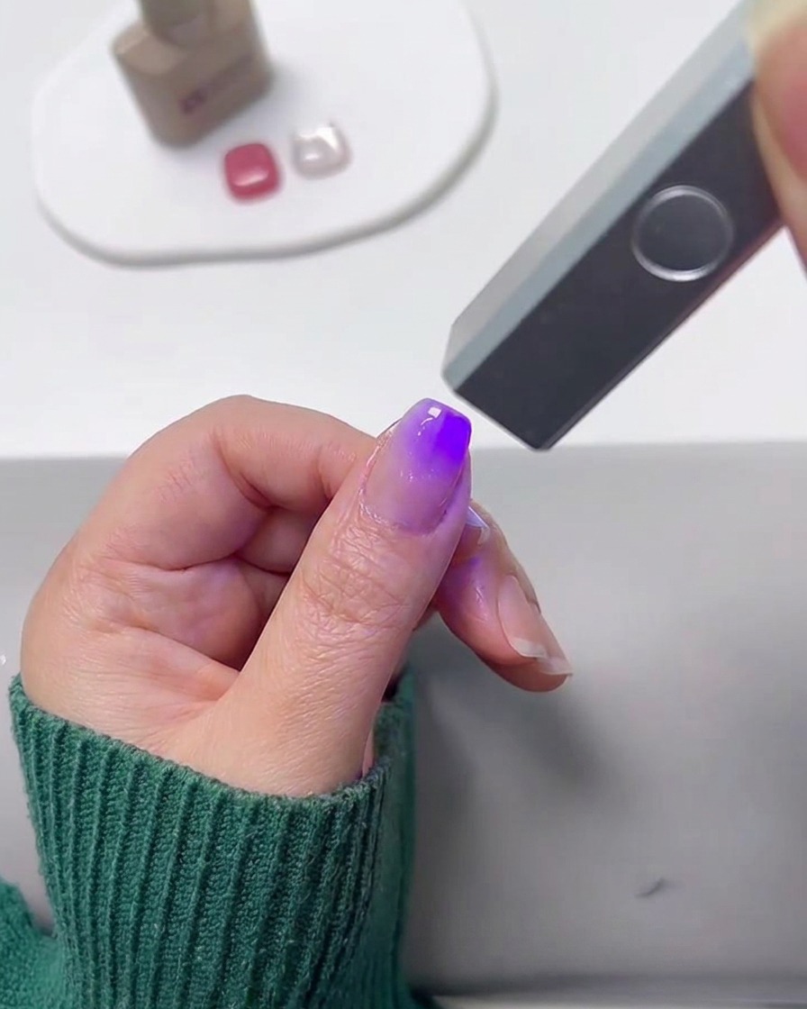 Une mini lampe UV catalysant un ongle peint en dégradé.