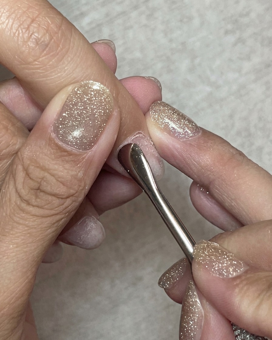 Gros plan dun repousse-cuticules en acier repoussant délicatement les cuticules sur un ongle naturel.