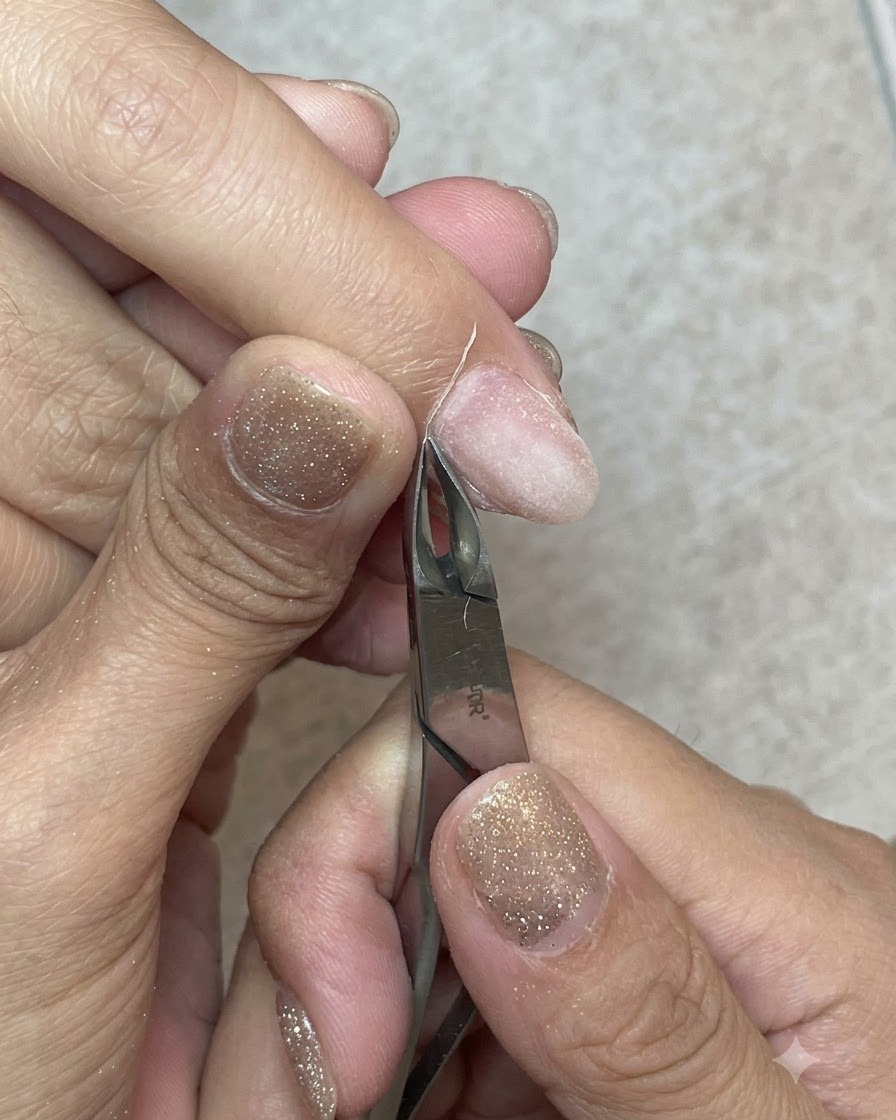 Une pince à cuticules en métal tranchante coupant nettement une bande de peau morte le long de la ligne des cuticules.