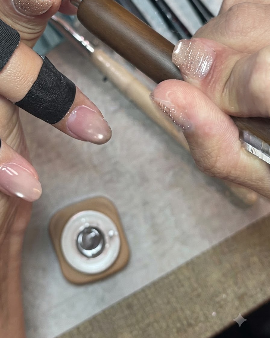 Une main tenant une mini lampe UV/LED positionnée directement au-dessus des ongles pour catalyser une couche de gel scintillant.