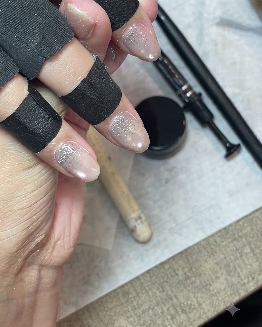 Une main portant des protège-doigts noirs utilisant un pinceau fin pour étirer et fondre le gel pailleté sur longle.