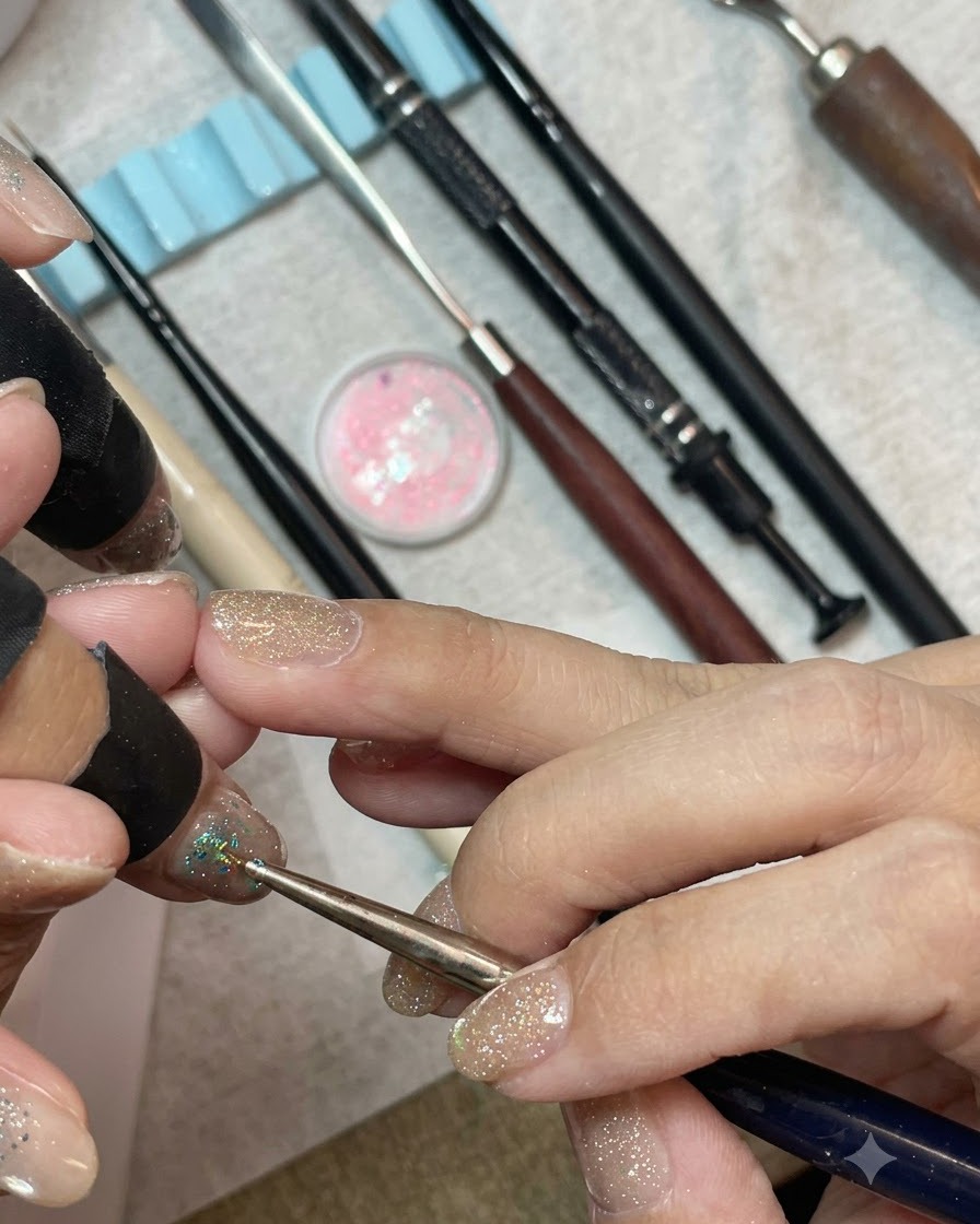 Un pinceau de détail posant densément des sequins hexagonaux bleu menthe et argentés sur le bout dun ongle vernis en gel.