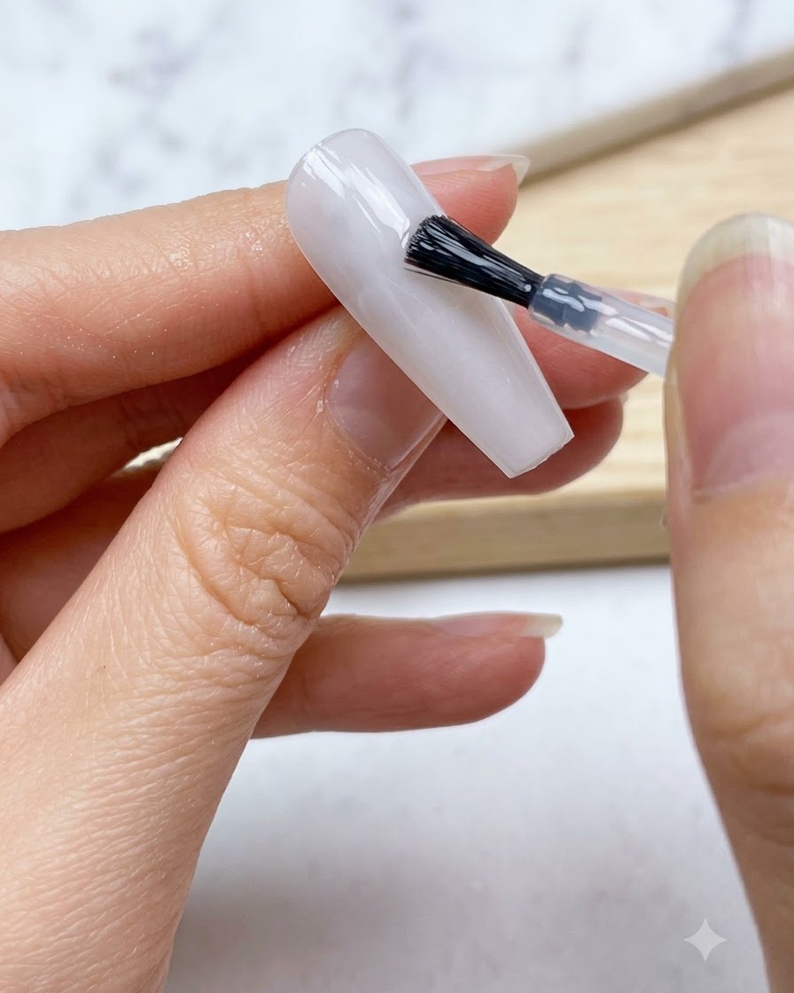 Un pinceau à ongle appliquant une couche lisse de base en gel blanc laiteux translucide sur tout longle.