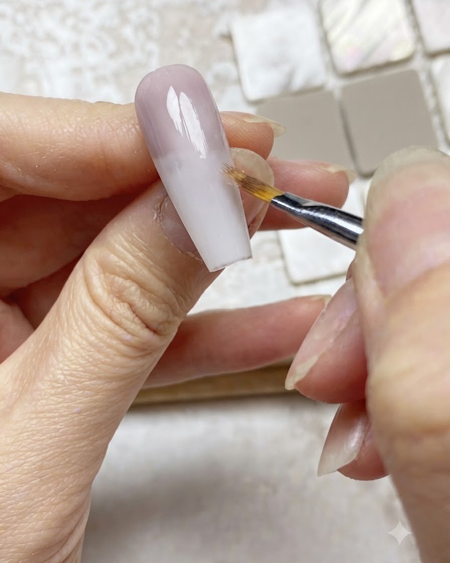 Un pinceau ombré estompant doucement le bord dune couche de gel violet vers le bas sur une extension dongle nude.