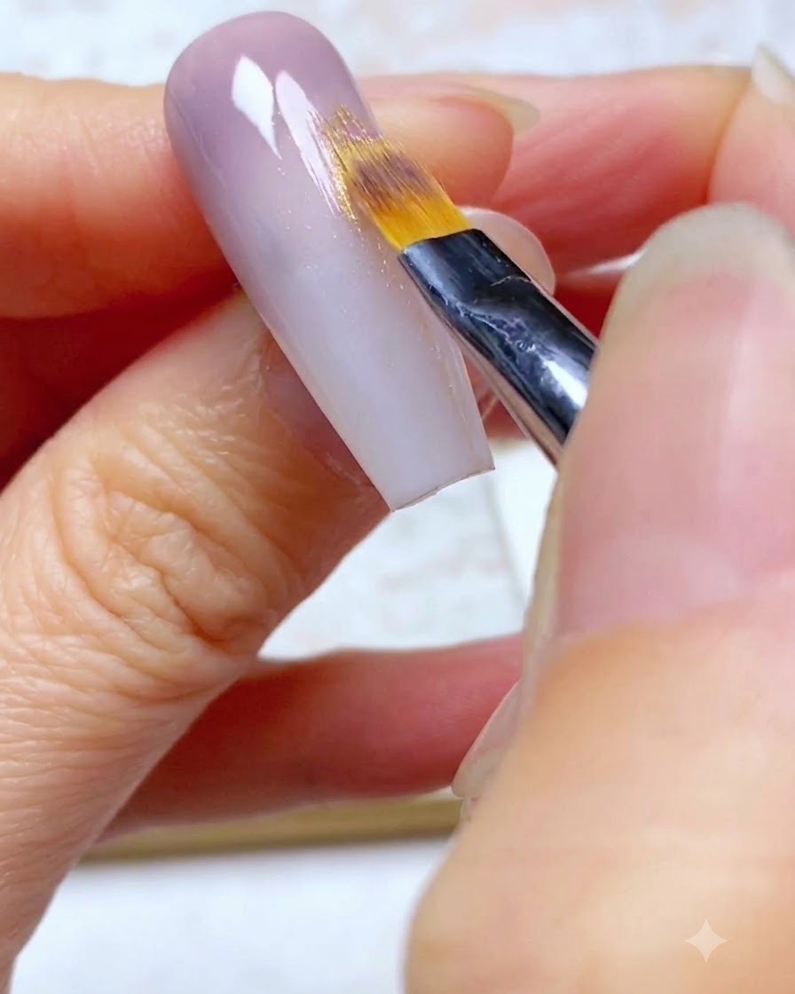 Un pinceau ombré estompant la deuxième couche de gel violet vers le bas sur longle.