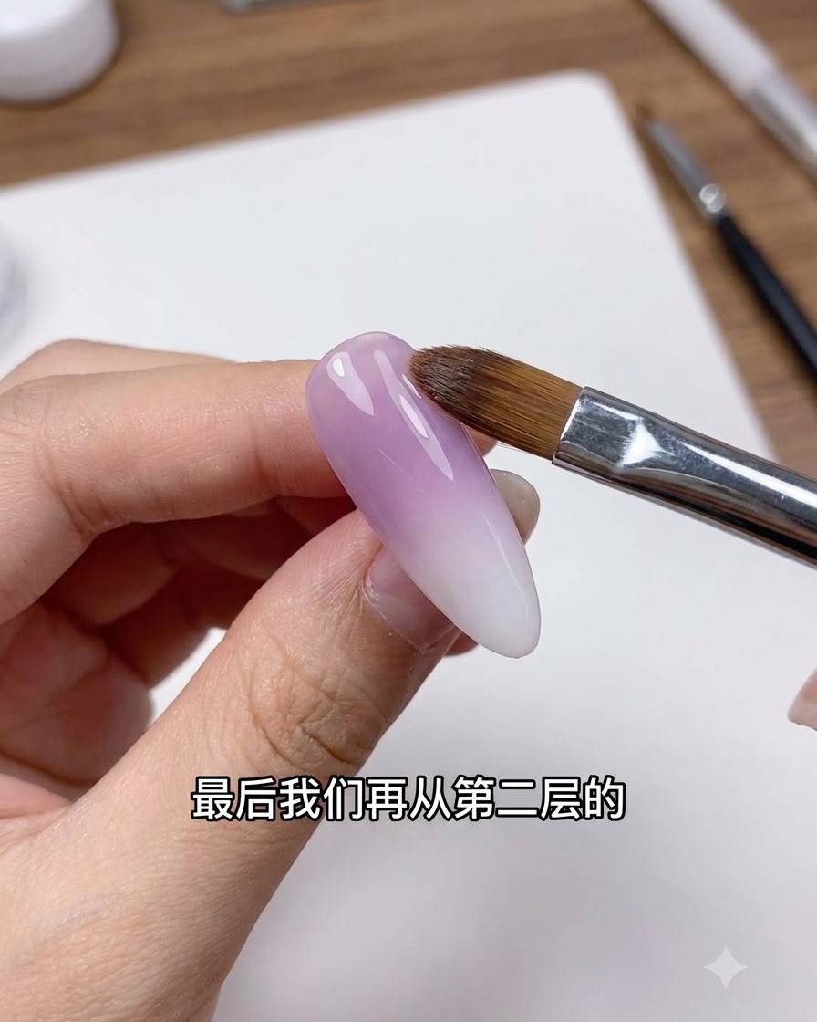 Un pinceau à ongle propre balayant délicatement la ligne de transition sur un ongle au dégradé violet et blanc.