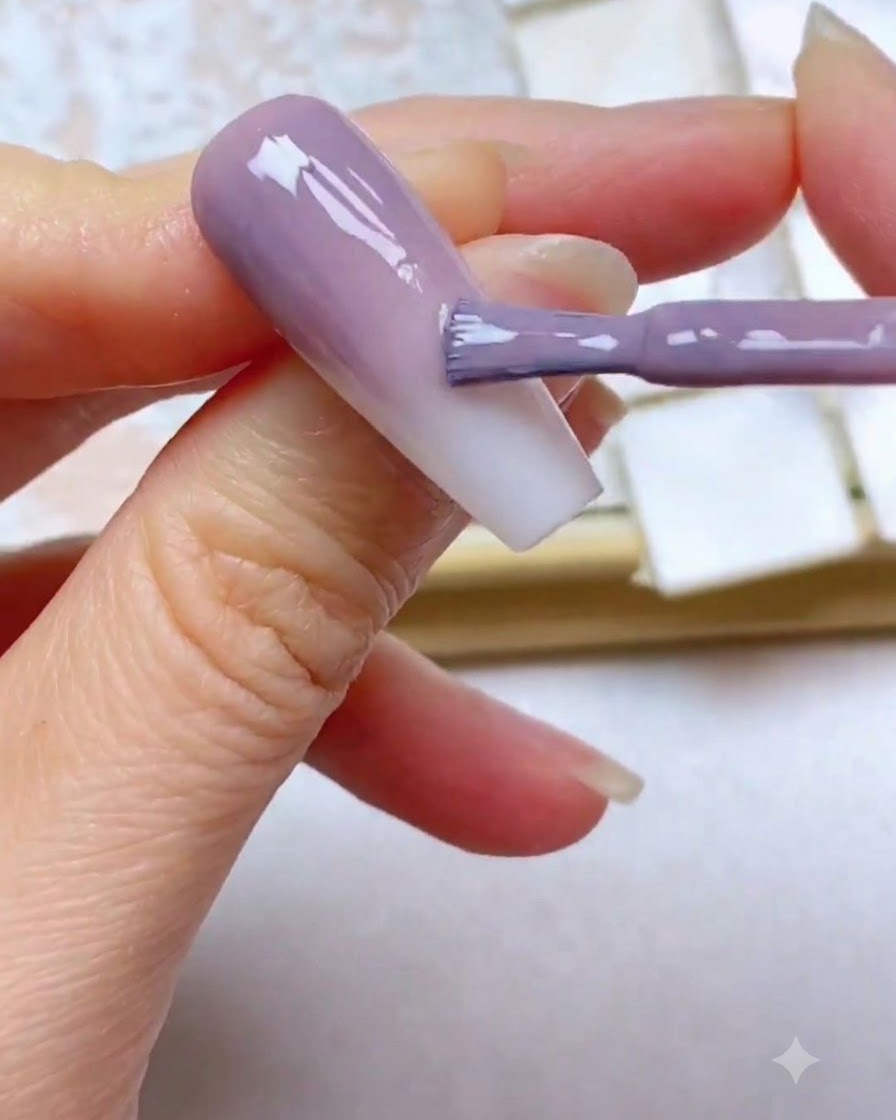 Un pinceau à gel appliquant une troisième couche de couleur violette près du bord supérieur de longle.