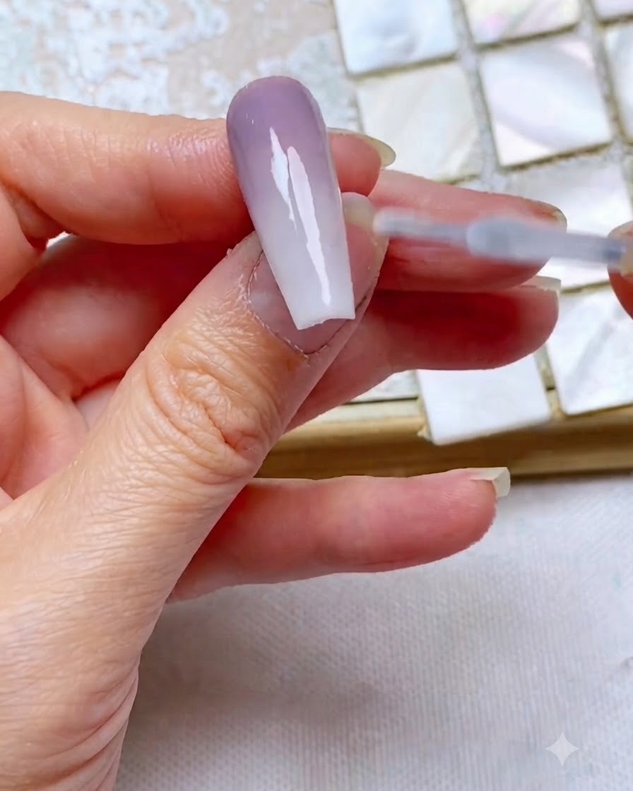 Un pinceau de top coat glissant en douceur sur un ongle en dégradé bicolore terminé pour sceller et ajouter de la brillance.