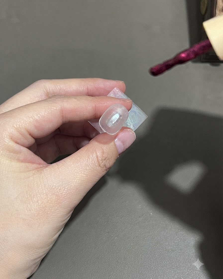 Un pinceau appliquant du vernis gel cat-eye violet foncé sur un ongle.