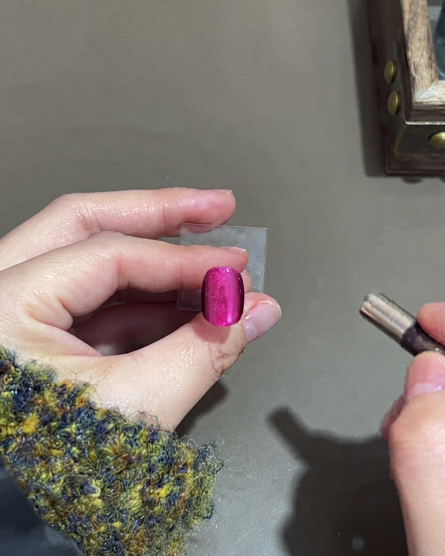 Un petit aimant cylindrique planant près dun ongle en gel cat-eye rose pour façonner le reflet.