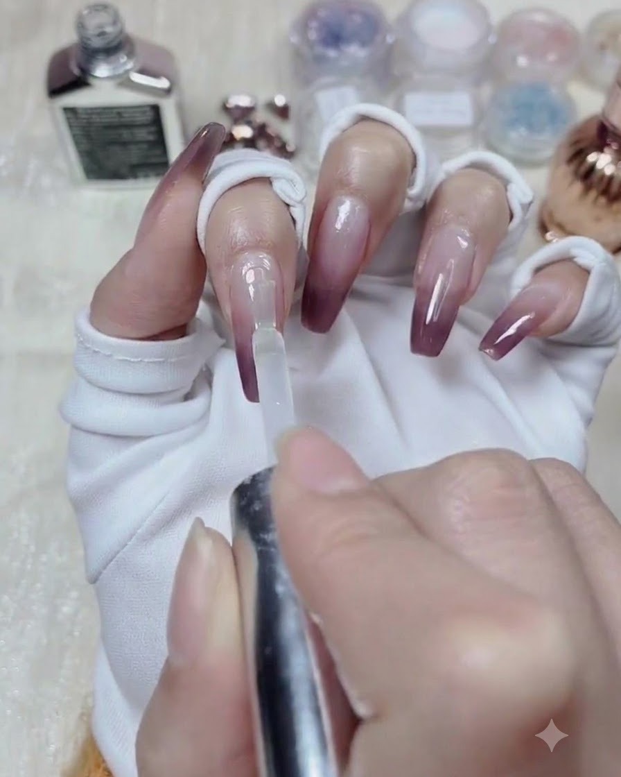 Un pinceau de flacon appliquant du gel de nivellement transparent sur toute la surface dun ongle peint en dégradé.
