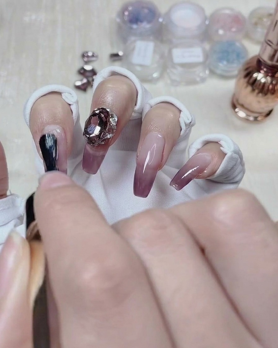 Une prothésiste ongulaire appliquant du top coat autour de la base dun cristal sur un ongle dégradé terminé.