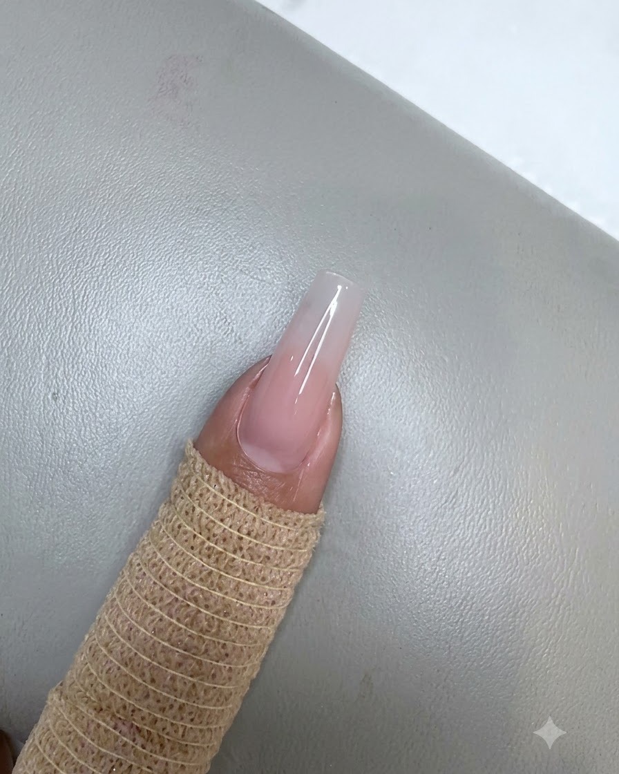 Un ongle avec une application de gel rose nude polymérisée sous une petite lampe UV LED violette.