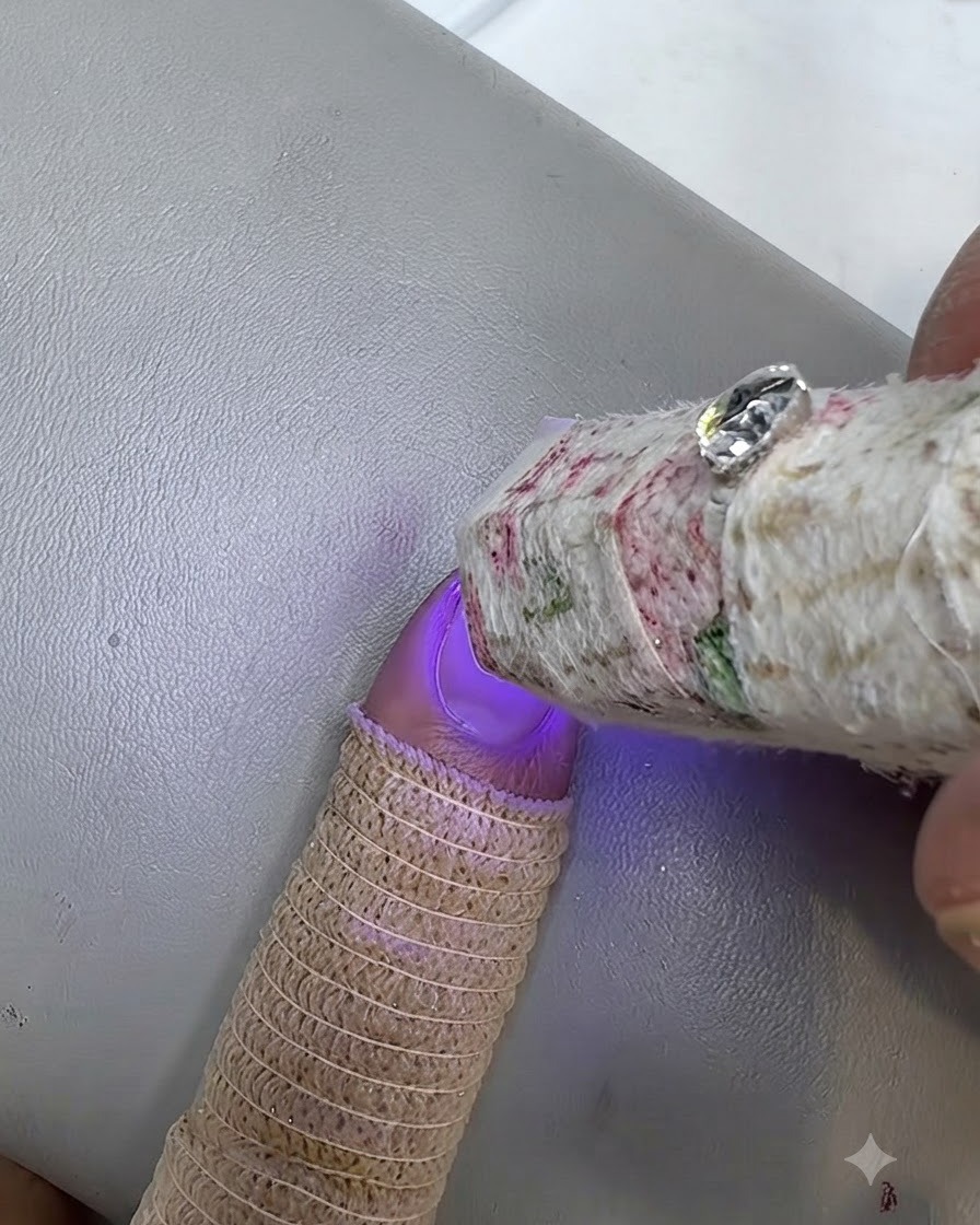 Une petite lampe UV catalysant un ongle verni dont le doigt porte un protège-doigt en tricot.