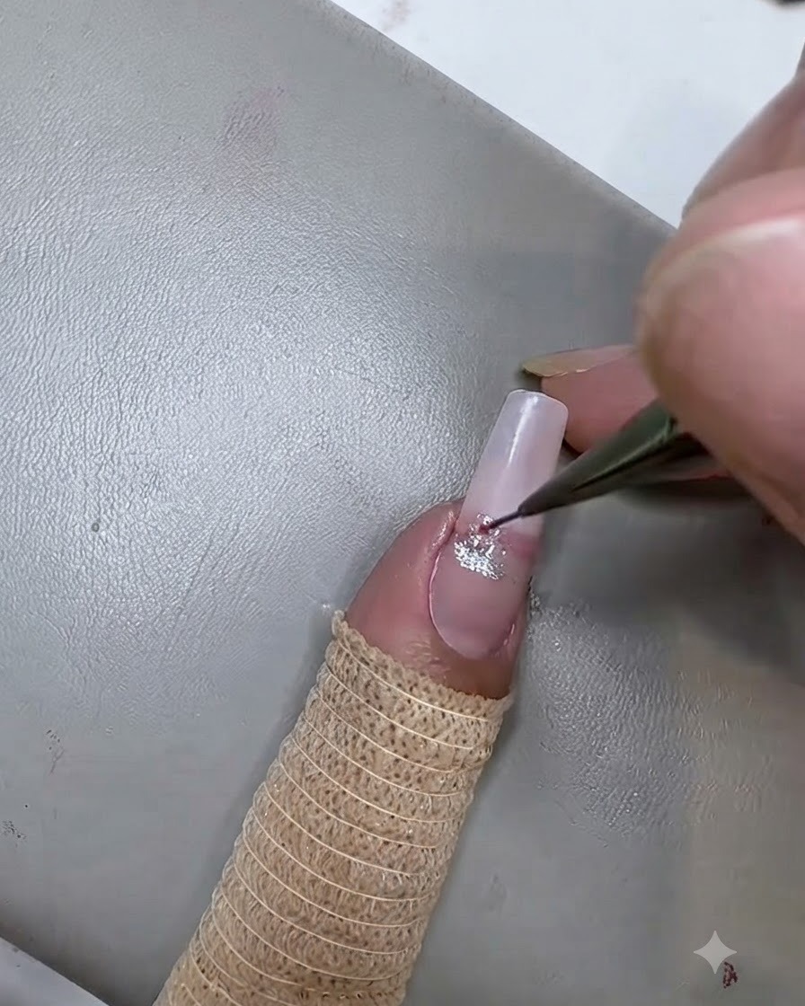 Un pinceau liner fin appliquant une deuxième rayure de gel cat eye rose sous la rayure argentée sur longle.