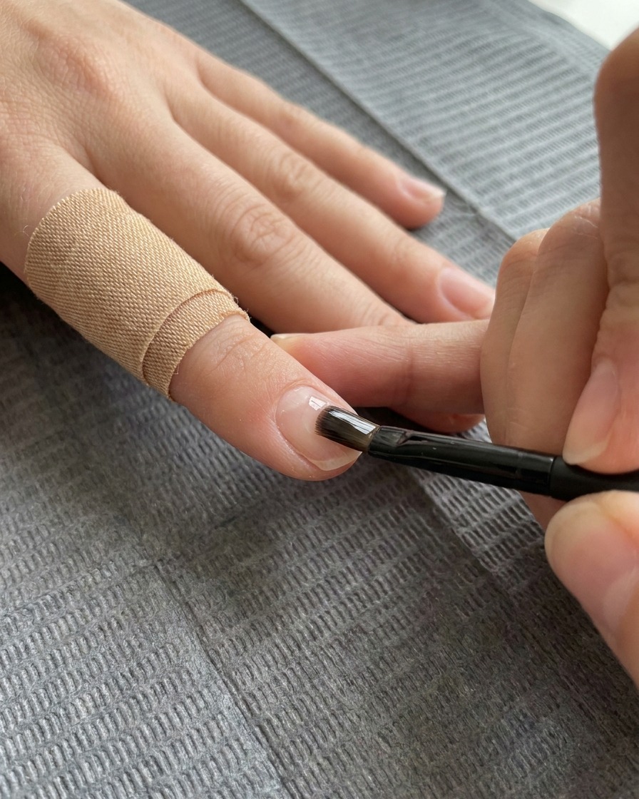 Un pinceau plat à gel appliquant une couche transparente de gel de renfort sur longle décoré.