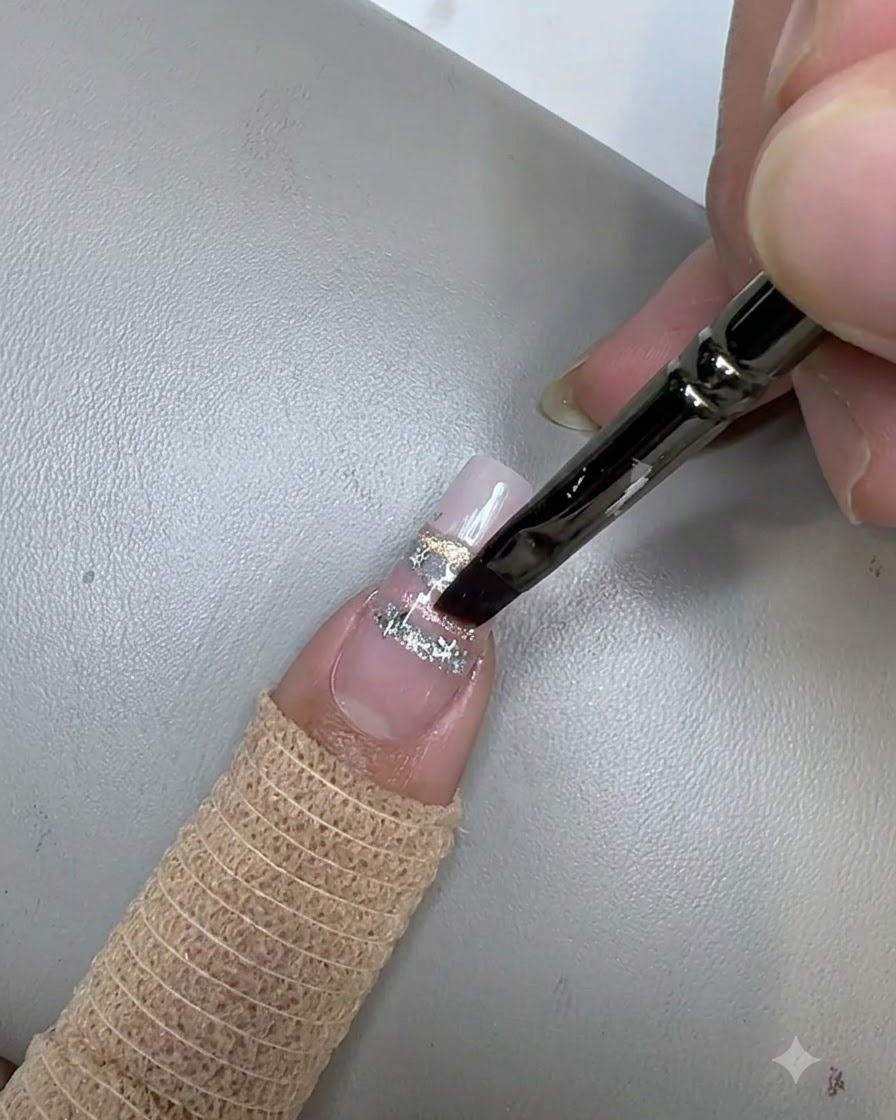 Un pinceau à ongles appliquant une couche de finition transparente sur des sequins étoiles sur un ongle décoré.