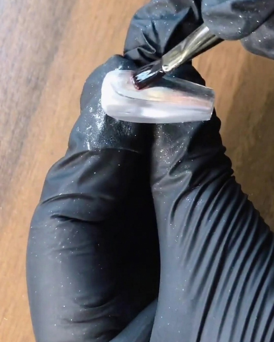 Un pinceau appliquant du gel de renforcement transparent sur un ongle chrome argenté.