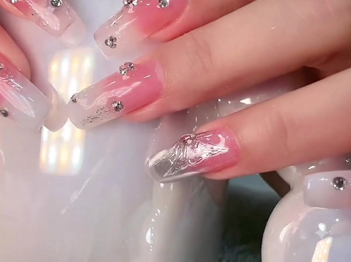 Gros plan de longs ongles carrés avec un dégradé blanc laiteux et des strass tenus contre une tasse en céramique blanche.