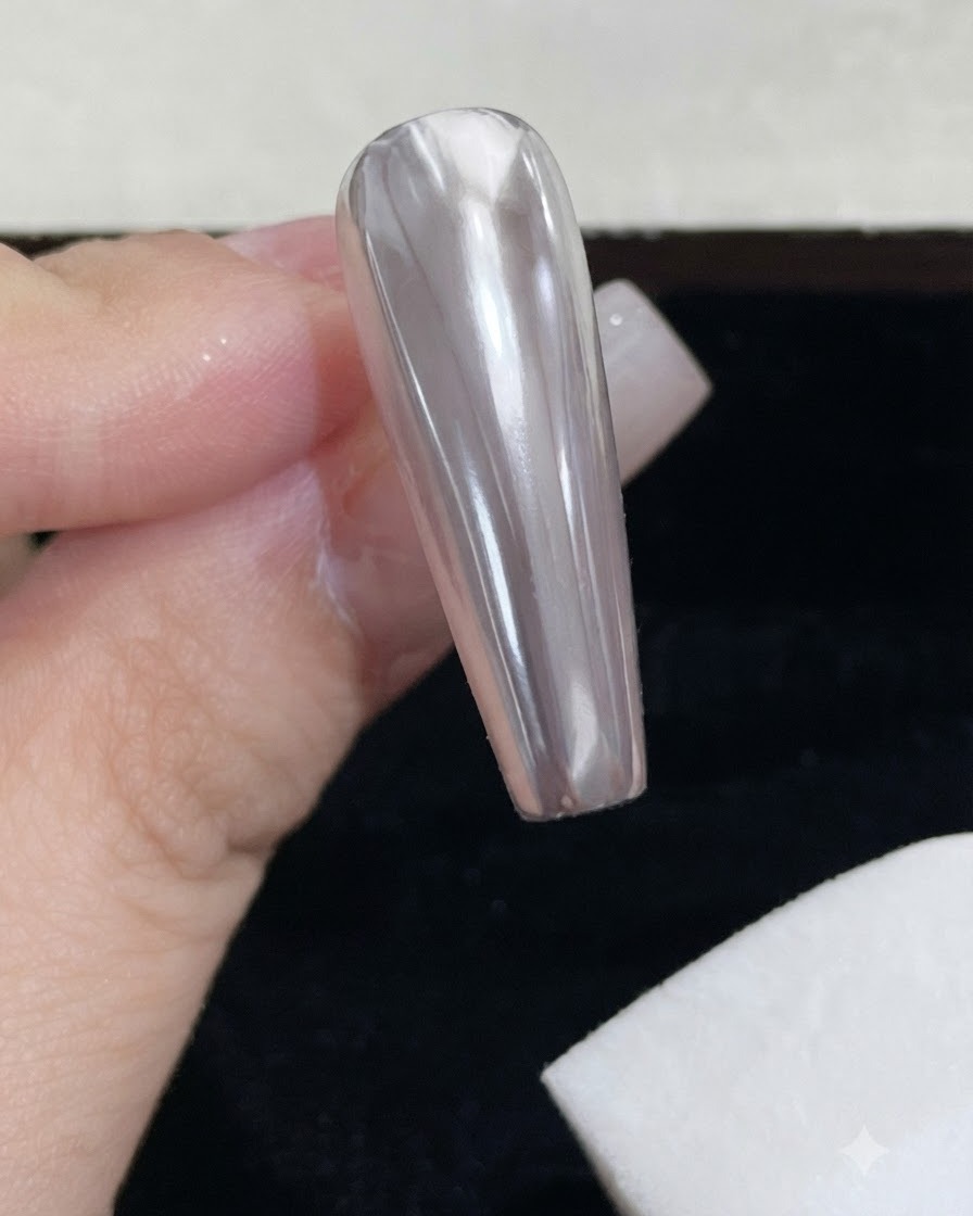 Un bloc déponge en mousse blanche essuyant lexcédent de poudre miroir sur un ongle chromé brillant.