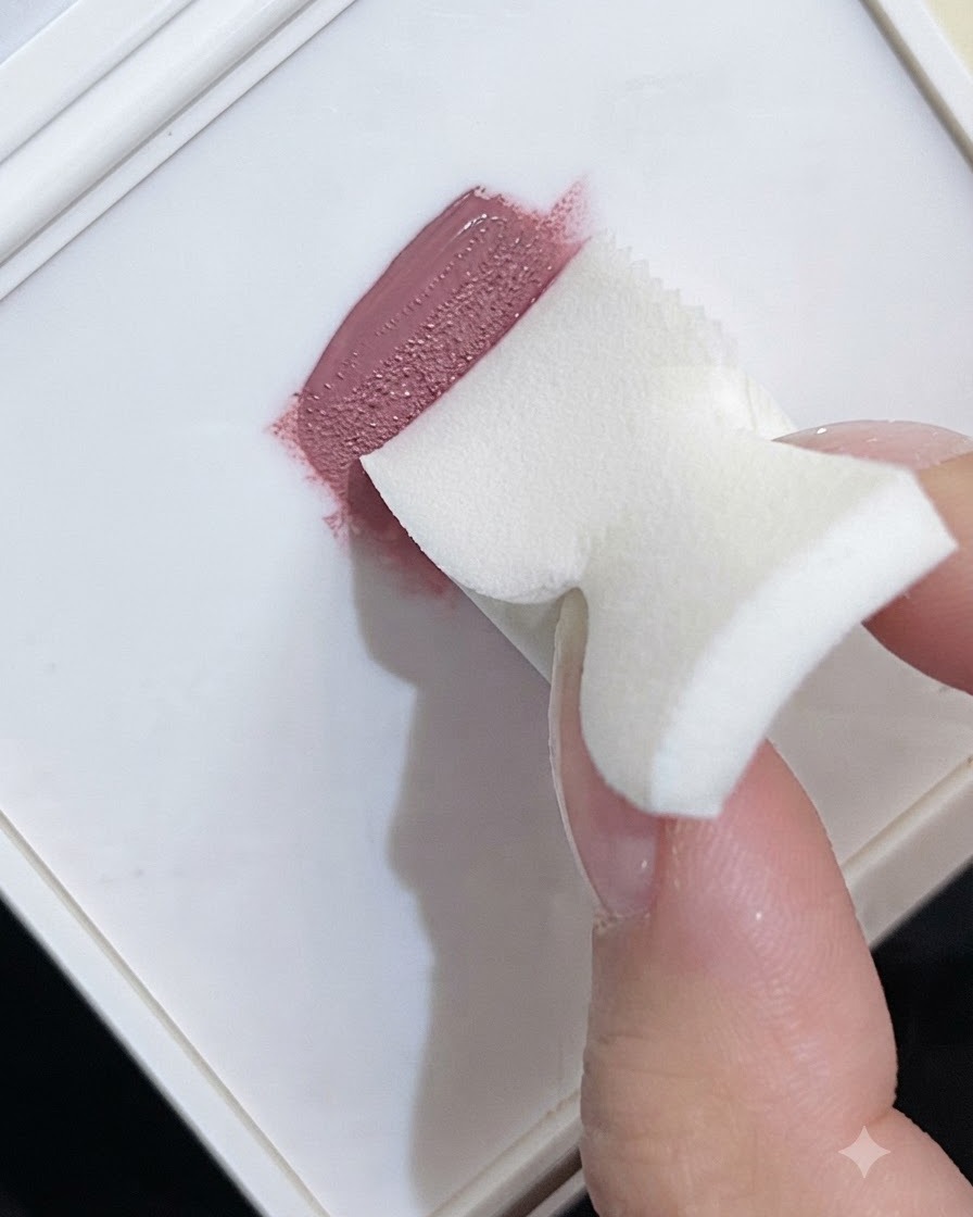 Une éponge à maquillage en mousse prélevant du vernis gel rose sur une palette pour créer une texture dégradée.