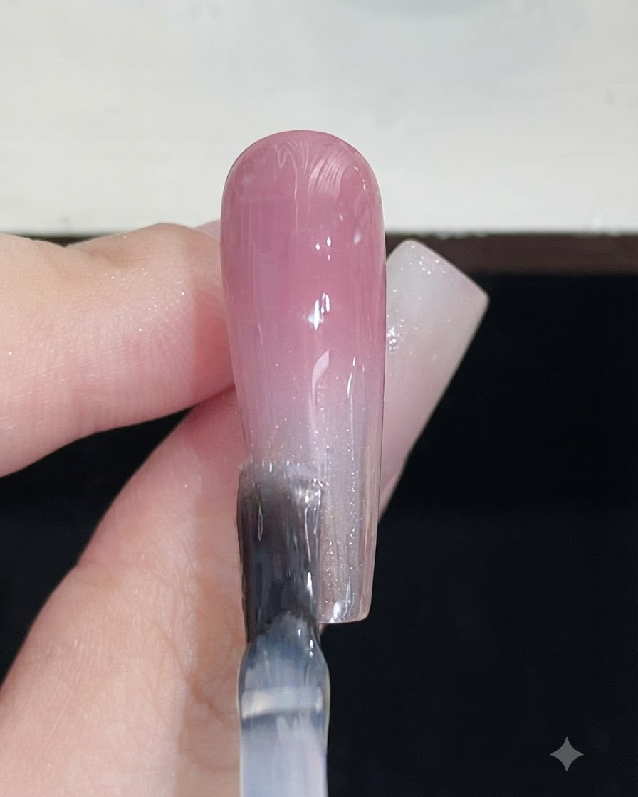 Un pinceau à ongles appliquant un top coat transparent sur un ongle au dégradé rose terminé.