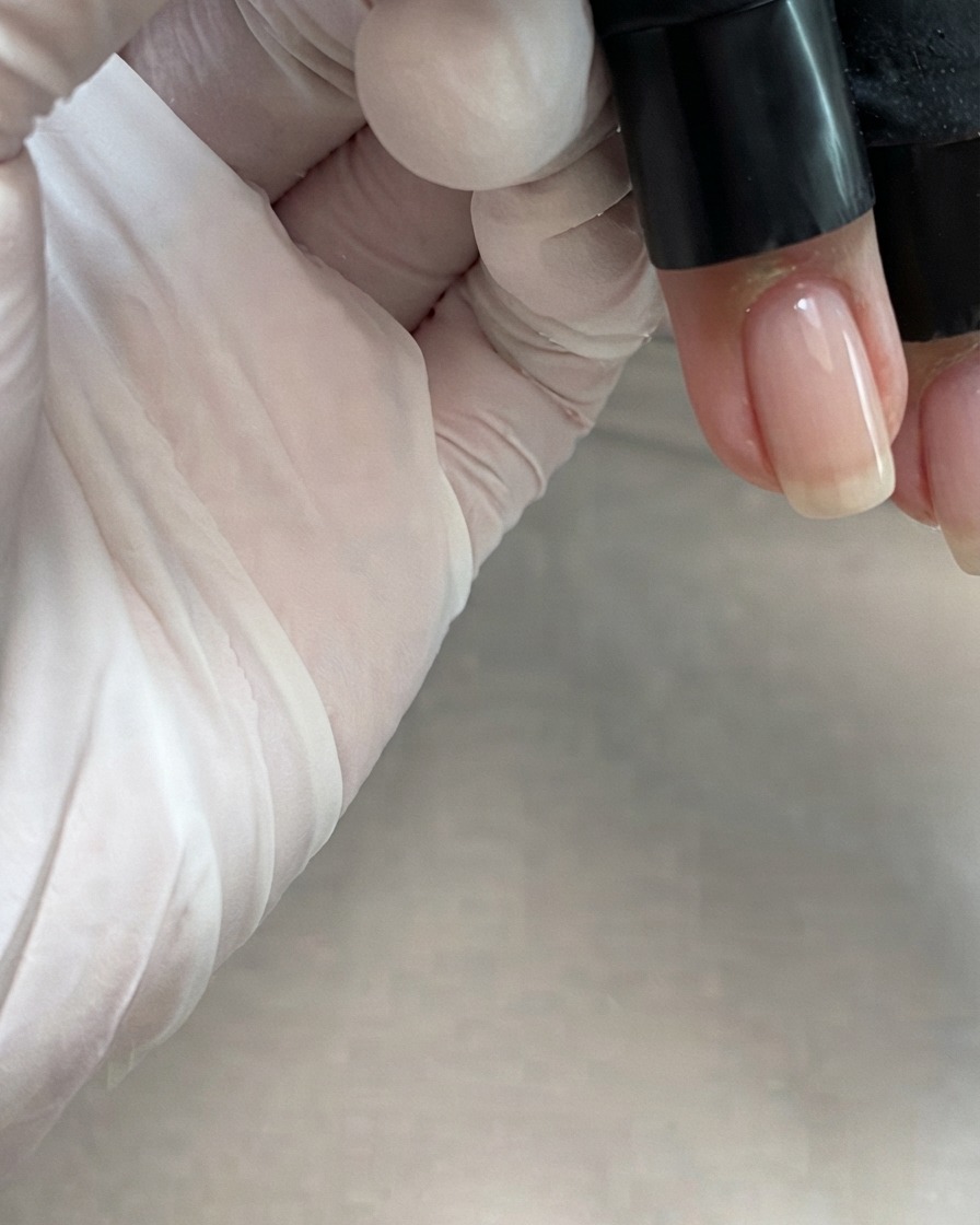 Un pinceau de flacon appliquant un gel de couleur rose nudé transparent au centre dun ongle.