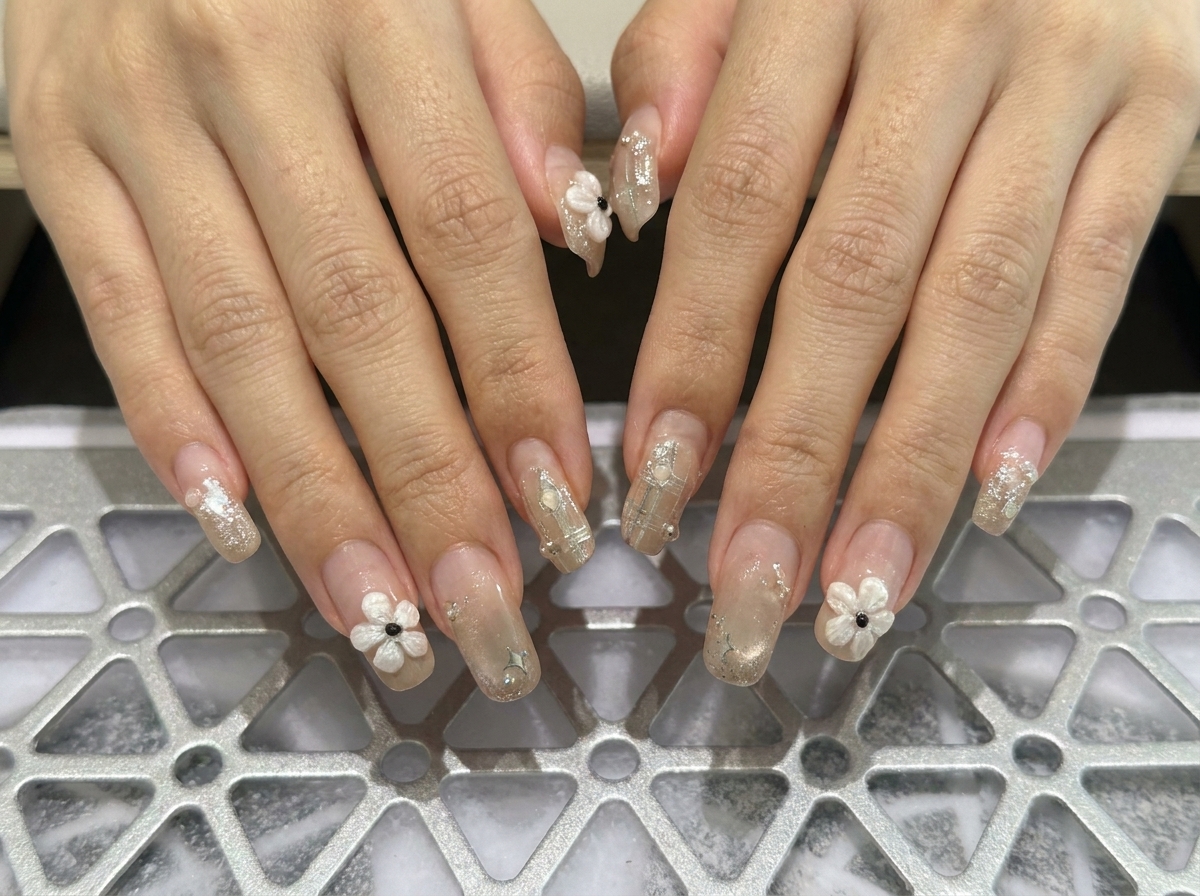 Macro centrée sur les doigts de la main gauche affichant des ongles carrés structurés ornés de délicates touches de perles.
