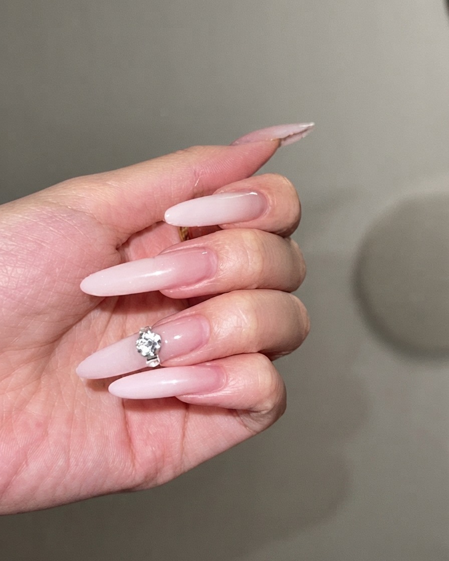 Un grand strass scintillant pressé au centre dun long ongle stiletto ombré blanc laiteux.