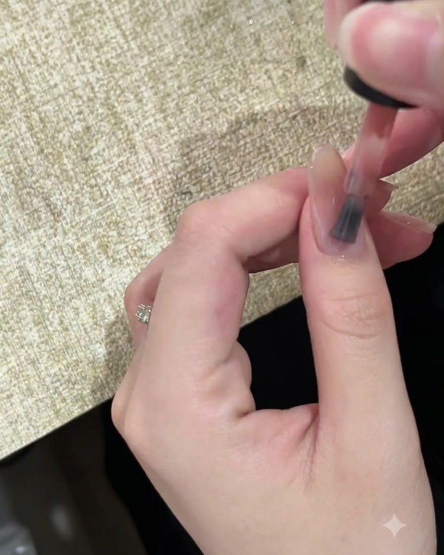 Gros plan dun pinceau appliquant un vernis gel nude diaphane sur un ongle naturel.