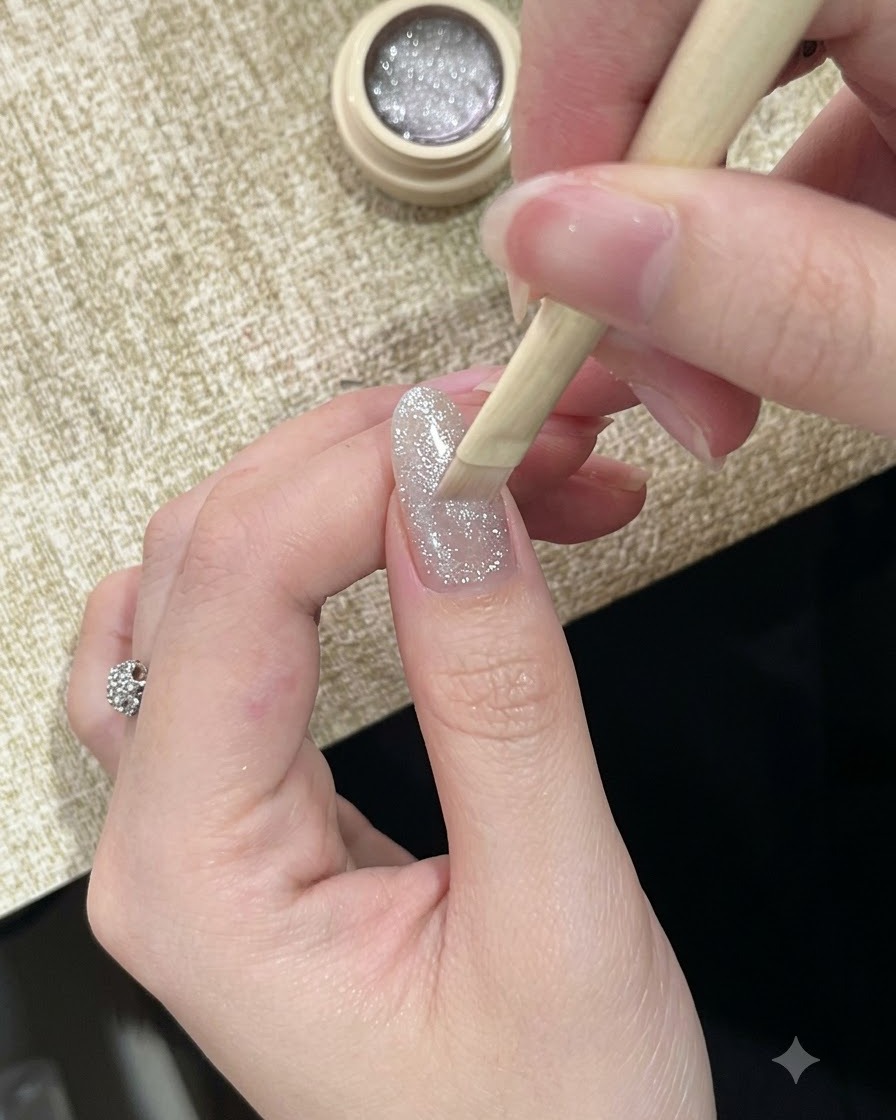 Un pinceau appliquant un vernis gel cat-eye argenté étincelant et hautement réfléchissant sur un ongle.