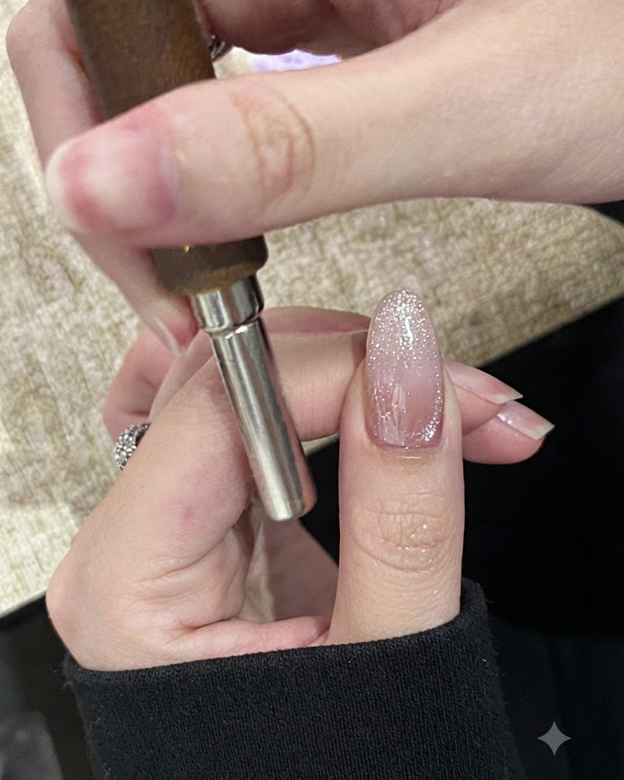 Une main tenant un aimant cylindrique horizontalement sur le bout dun ongle non catalysé peint avec un gel cat-eye scintillant.