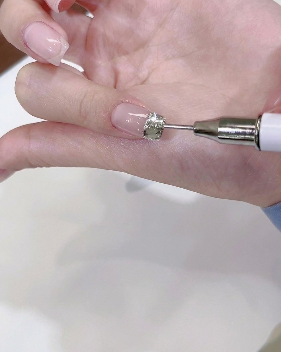Un outil de dotting fin plaquant de minuscules billes dacier et mini cristaux autour dun grand strass central sur un ongle.