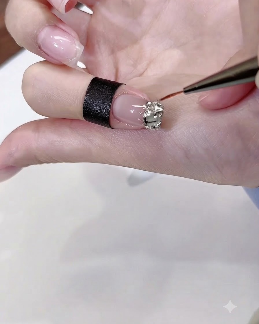 Un pinceau fin de nail art appliquant précisément de la colle gel diamant transparente autour des bords dun groupe de strass sur un ongle poli.
