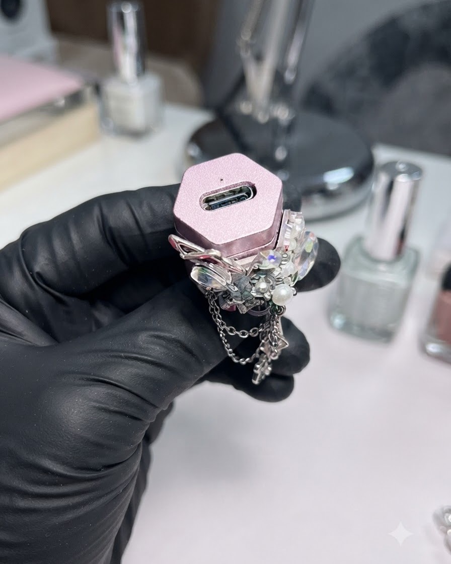 Une main gantée tenant une petite lampe UV/LED rose décorée de strass.