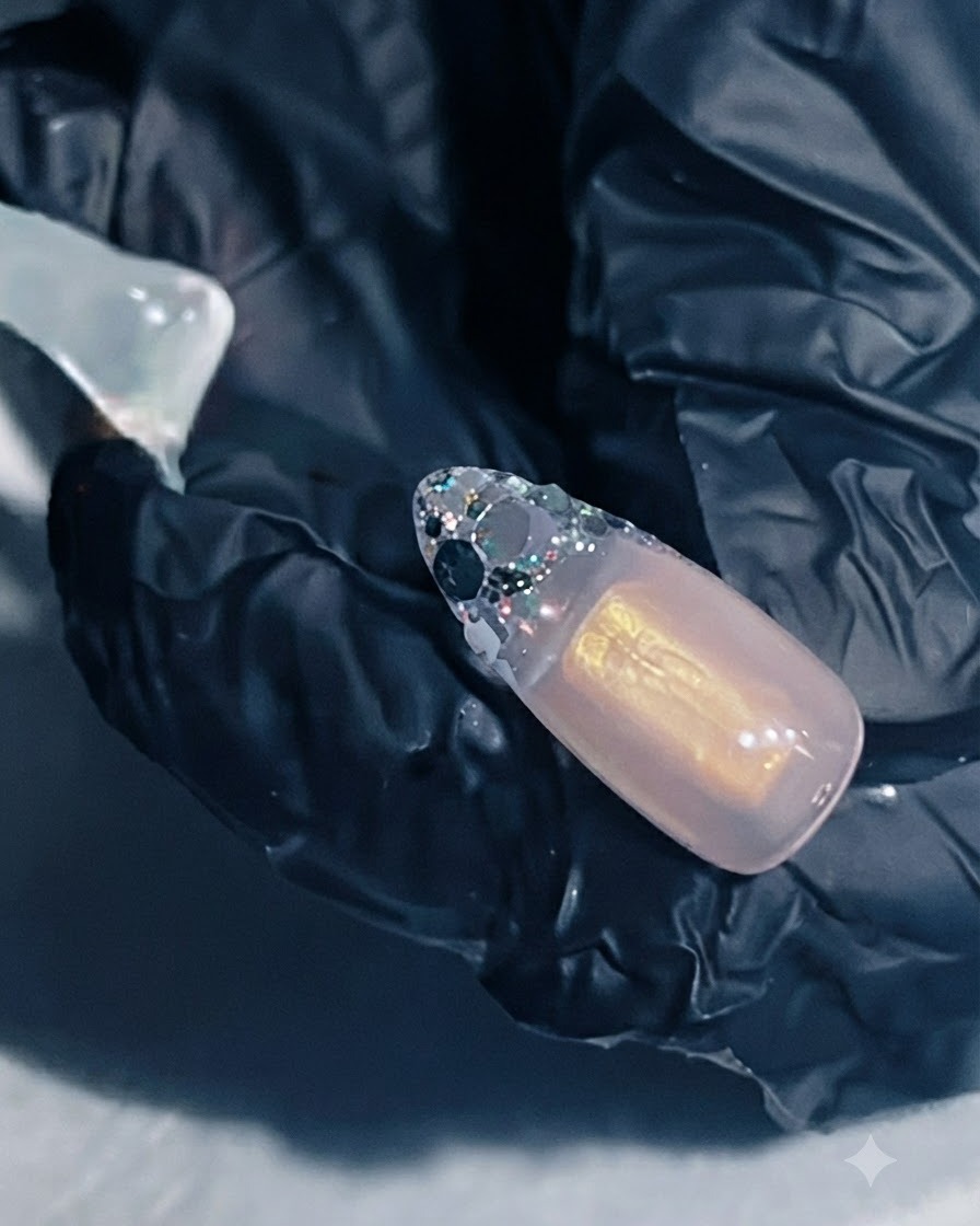 Une main tenant une extension dongle avec du gel de renforcement appliqué sur la zone de la French pailletée.