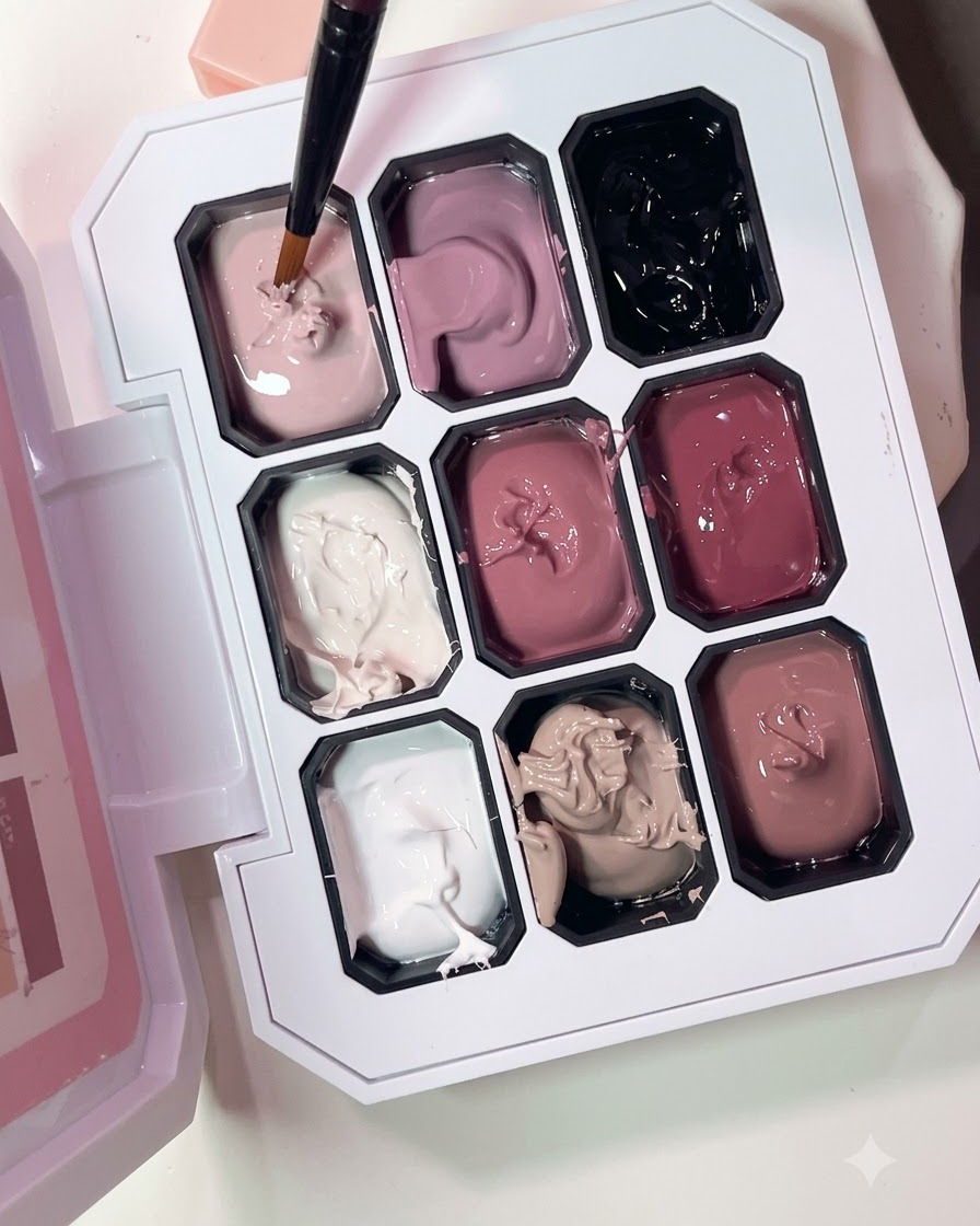 Un pinceau fin prélevant du gel rose nude dans une palette à plusieurs compartiments.