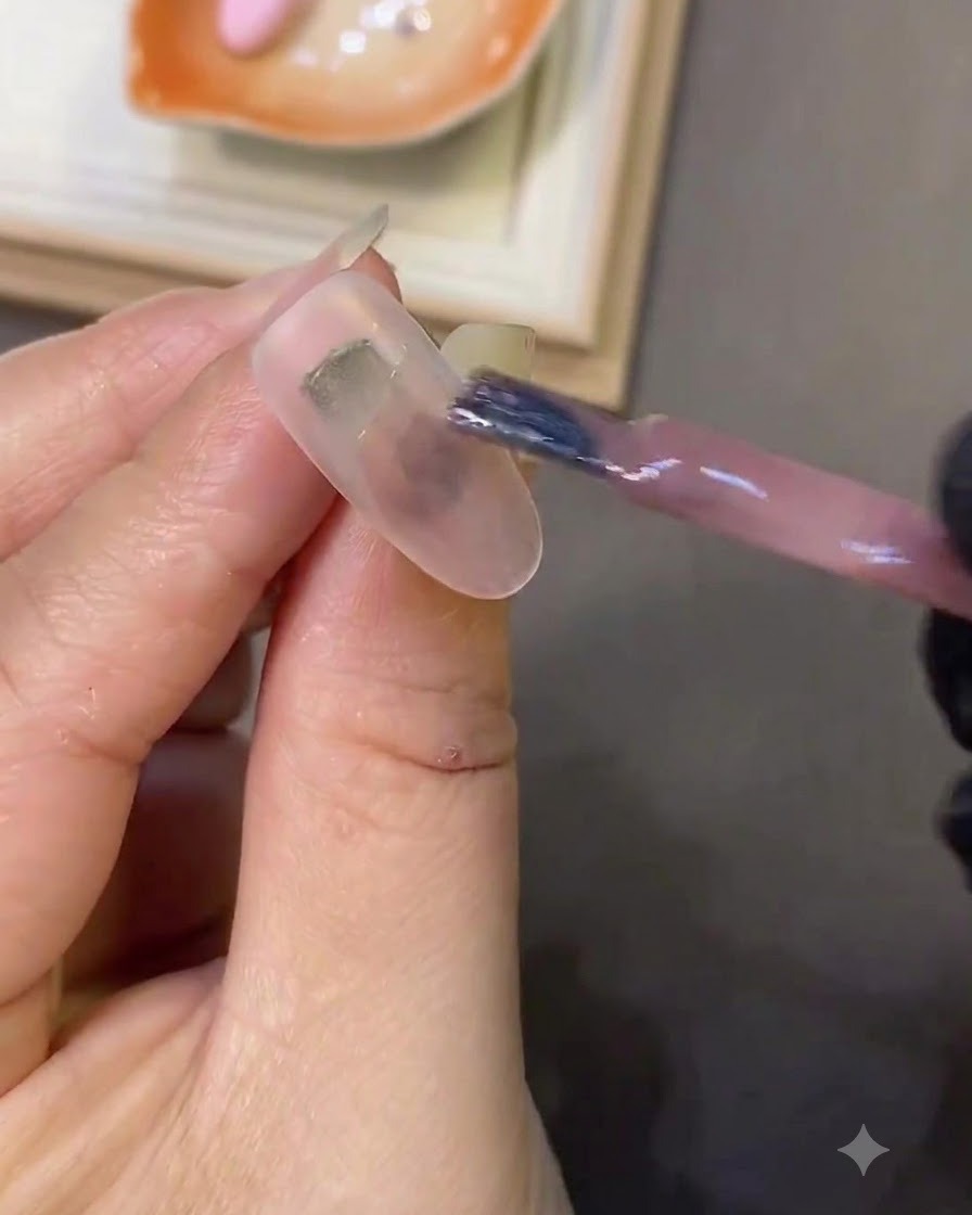 Un pinceau appliquant du gel œil-de-chat rose clair sur un ongle blanc laiteux.