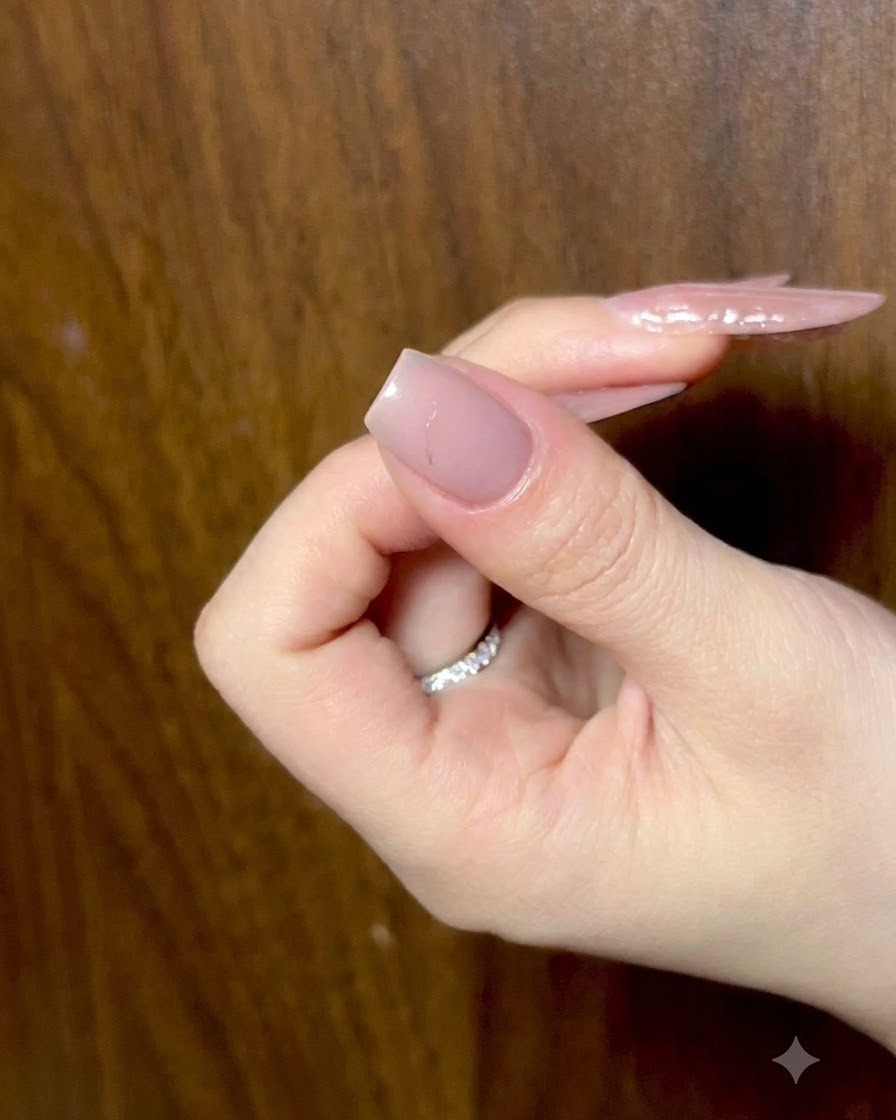 Une main au repos avec les doigts légèrement repliés, montrant des ongles nude préparés sous un éclairage ambiant.