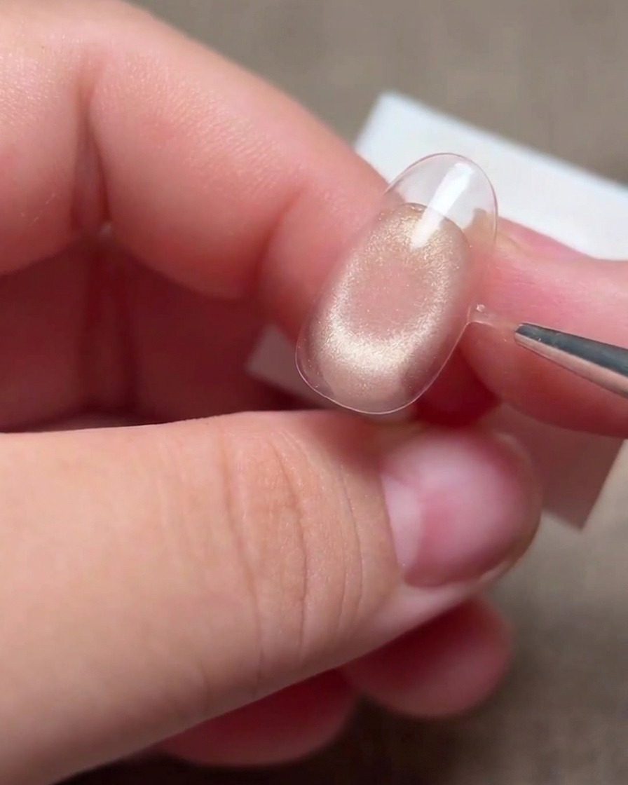 Une main utilisant un pinceau liner fin pour retoucher les contours de la ligne de sourire sur lextrémité dun ongle.