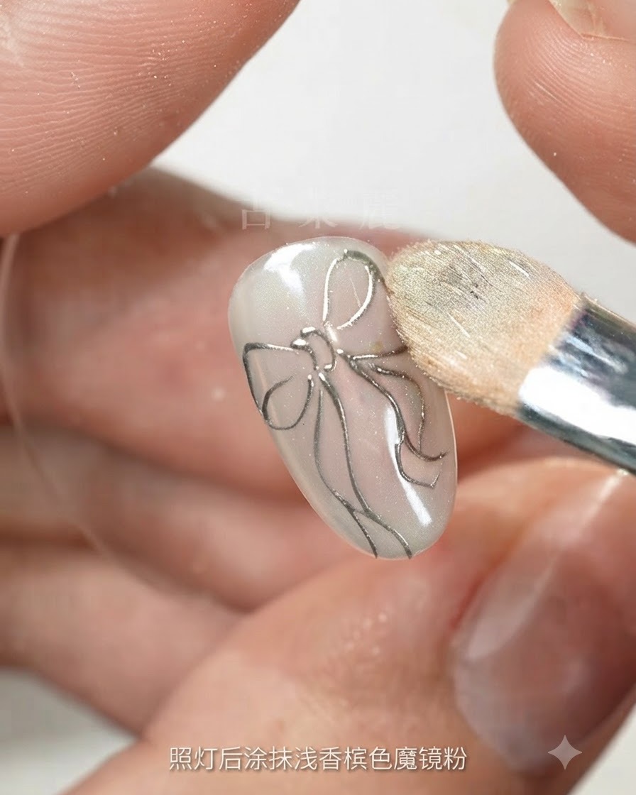 Une éponge de maquillage estompant de la poudre magique champagne clair sur un ongle doté dun contour de nœud argenté.
