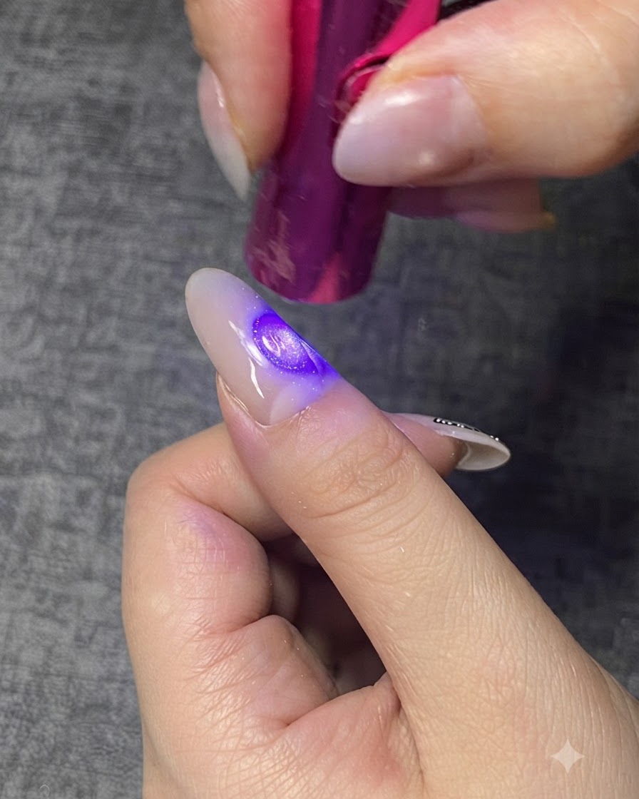 Une mini lampe UV/LED violette catalysant une couche de gel transparent sur un ongle.