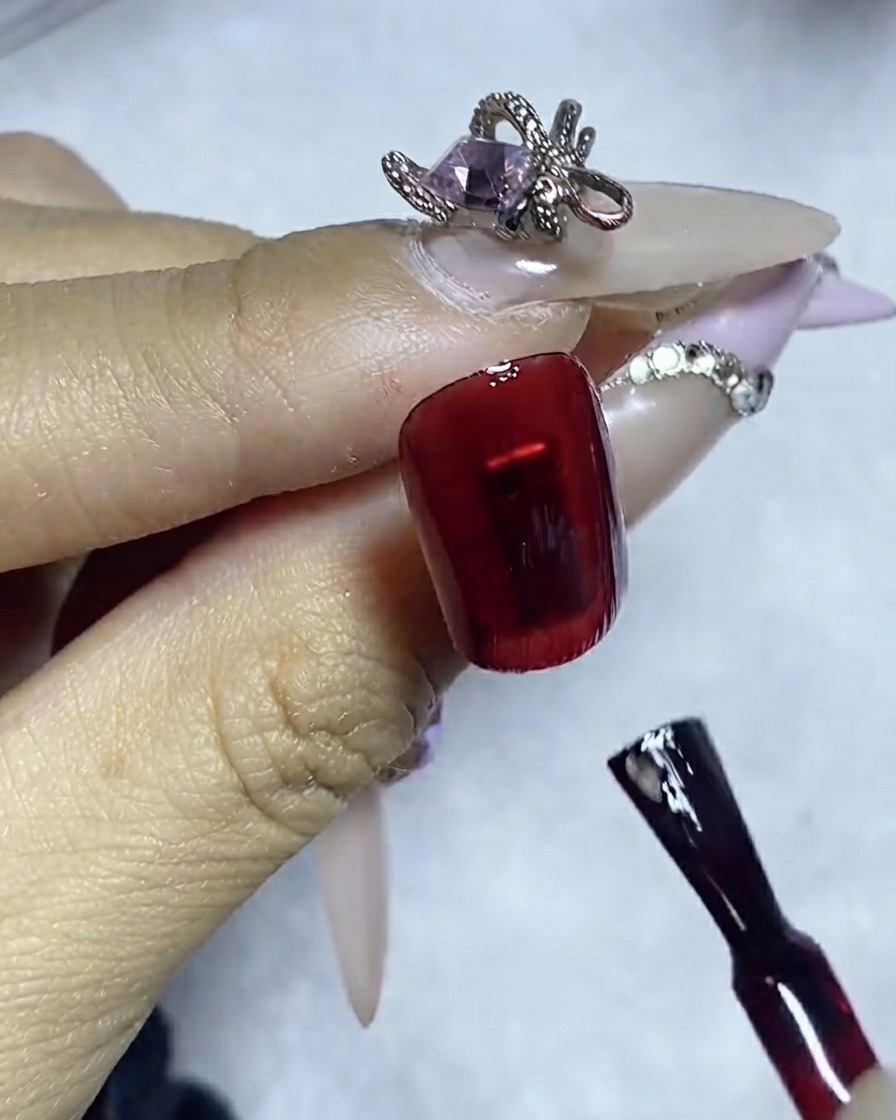 Un pinceau liner appliquant une ligne précise de colle à strass sur la surface dun ongle rouge foncé.