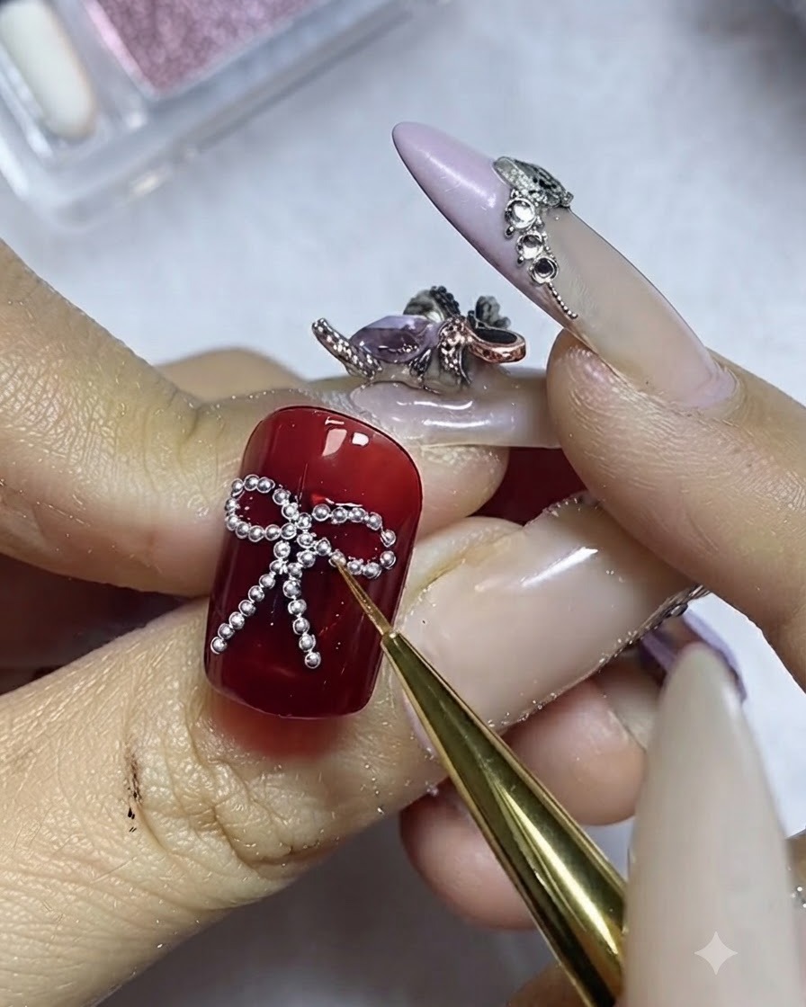 Un pinceau fin appliquant délicatement du top coat autour du périmètre des billes dacier argentées sur un ongle rouge.
