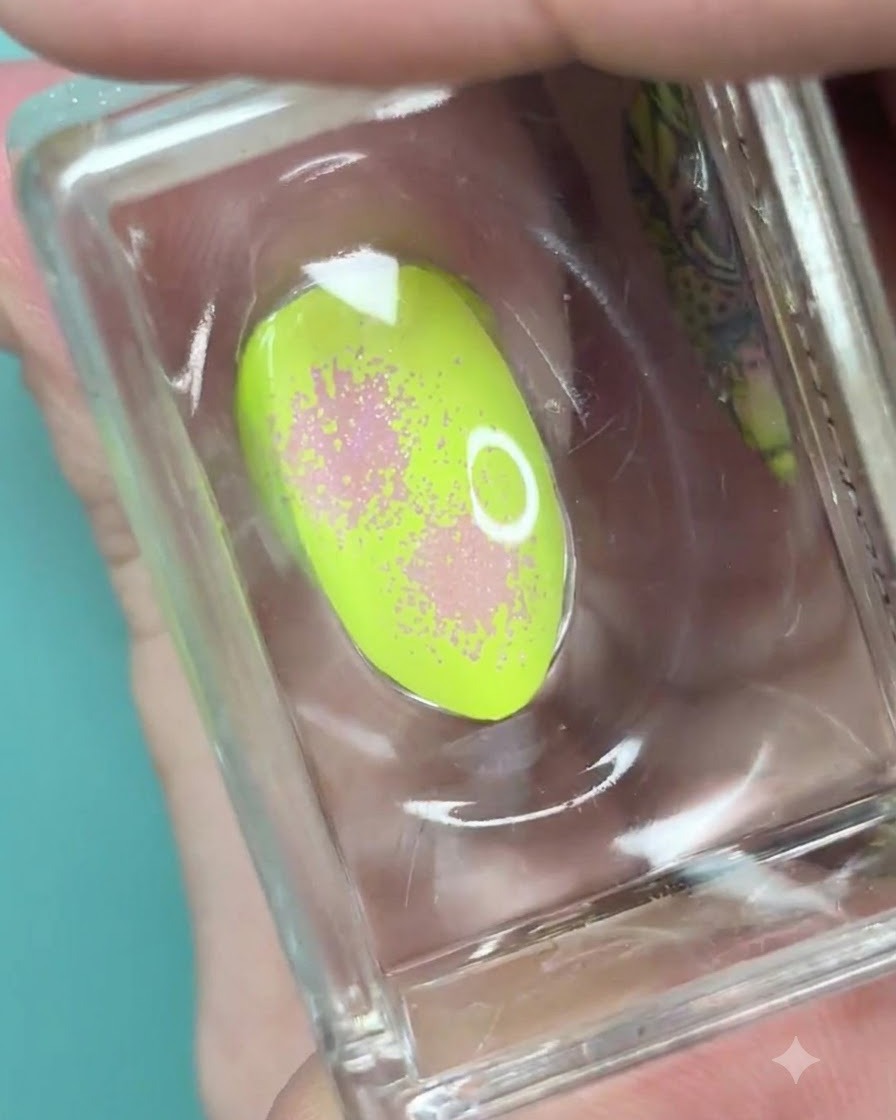 Un tampon en silicone transparent tenant un ongle vert néon avec un dégradé rose doux et une texture pointillée.